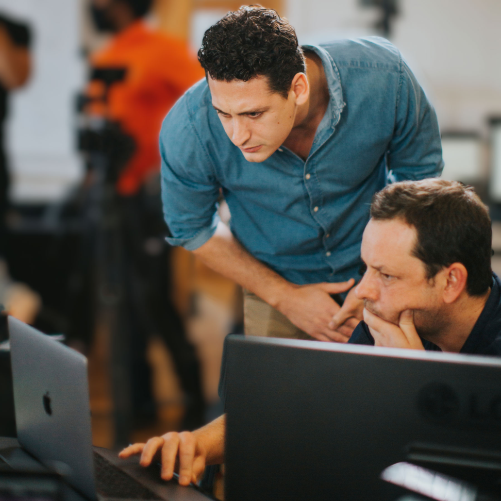 A person sitting down and using a laptop while another person is standing and looking at the laptop