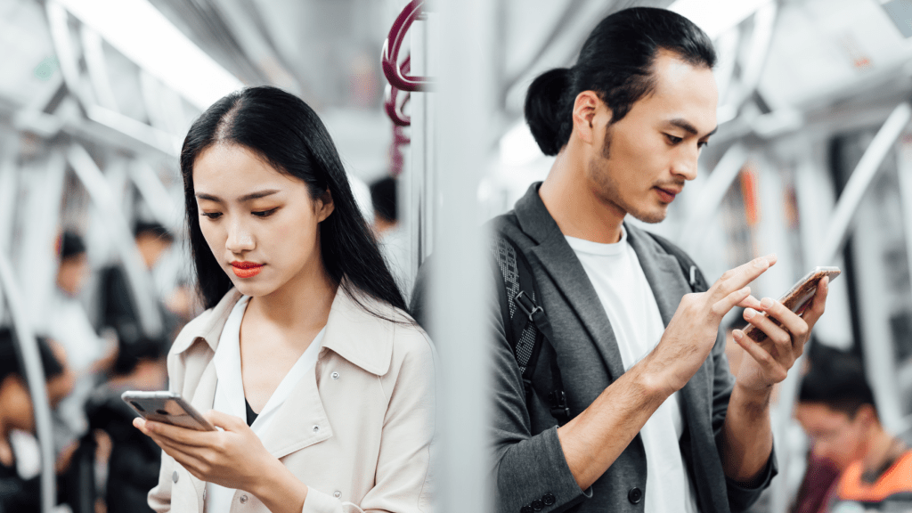Two individuals back-to-back on public transportation looking down at their cell phones