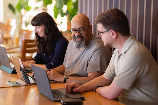 Three persons sitting at a desk with their laptops. 